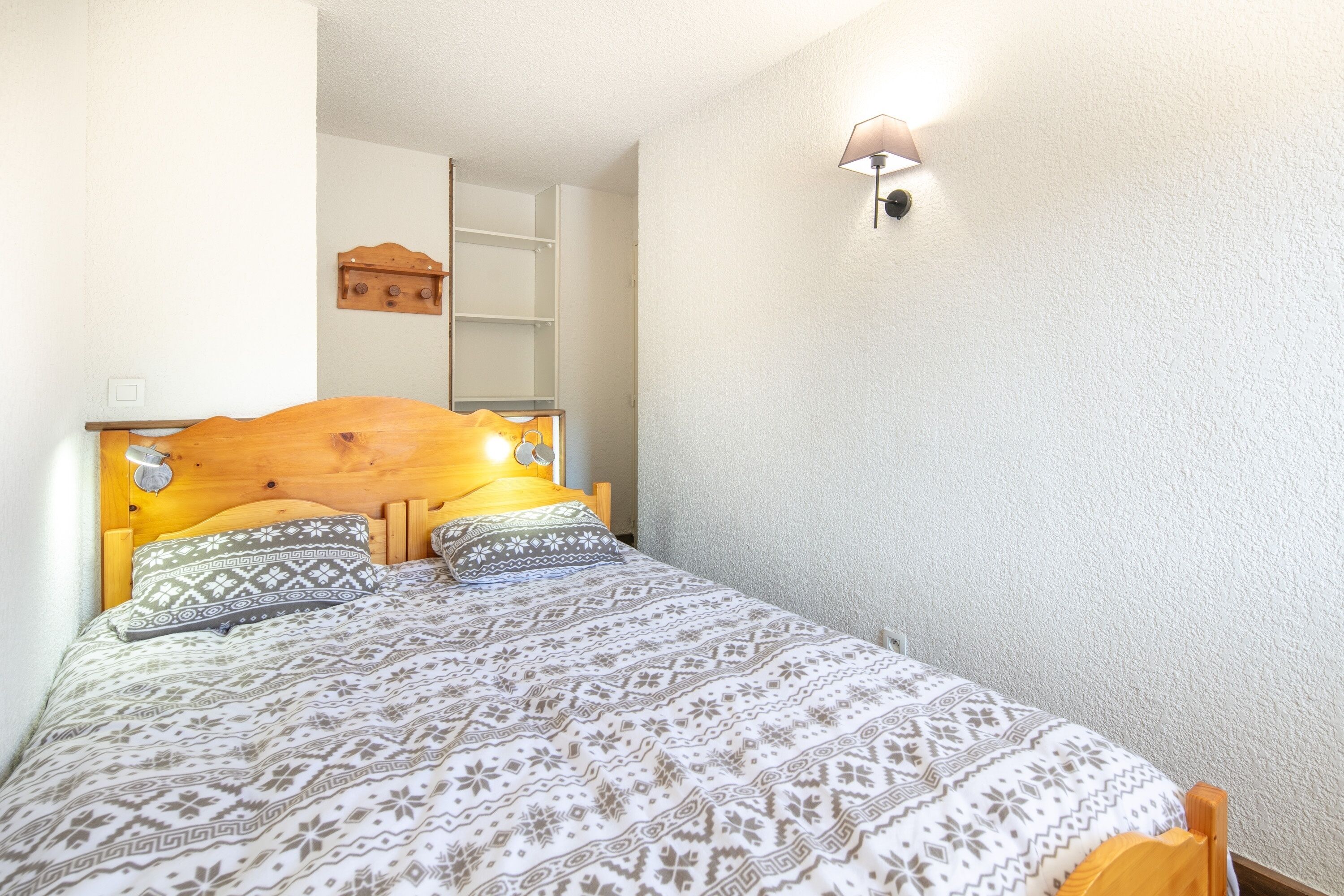Une chambre à coucher avec une tête de lit en bois, une literie à motifs, une lampe de chevet et un luminaire fixé au mur.