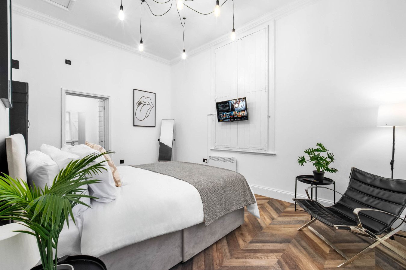 Ein modernes Schlafzimmer mit Bett, Fernseher, Sessel und einer Topfpflanze.