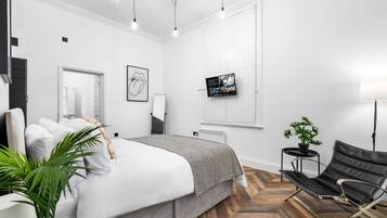Ein modernes Schlafzimmer mit Bett, Fernseher, Sessel und einer Topfpflanze.