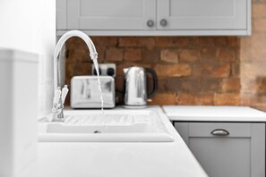 A kitchen with a white sink, a faucet, a toaster, and a kettle on a countertop.