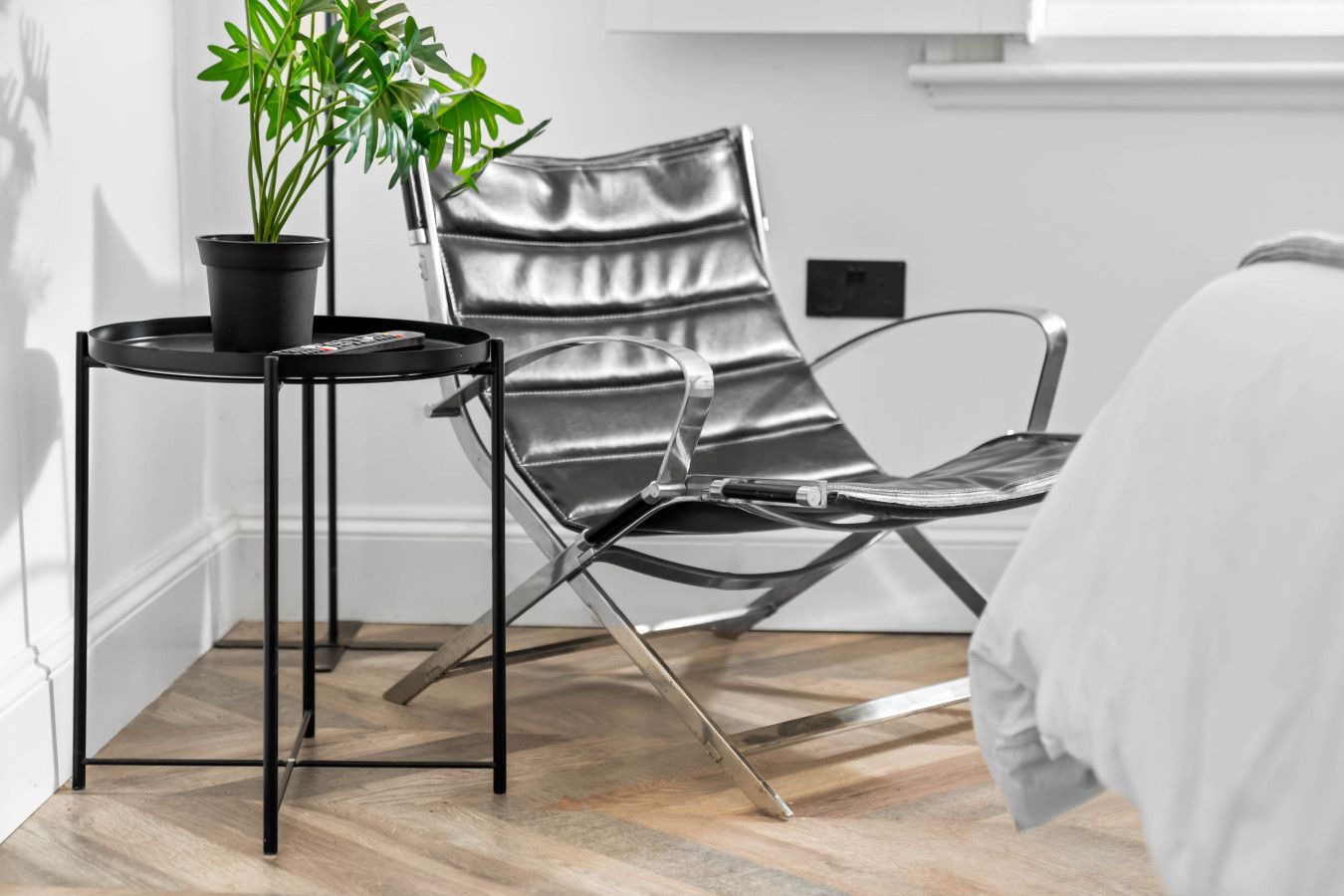 A room with a leather chair, a small table with a potted plant, and a bed.