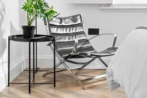 Een kamer met een leren fauteuil, een bijzettafeltje met een plant in pot en een bed.