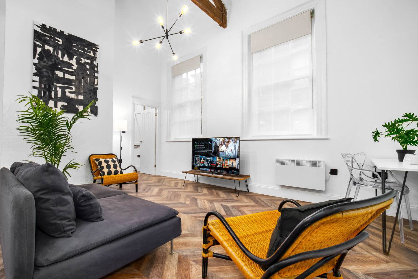 Ein modernes Wohnzimmer mit einem grauen Sofa, einem gelb-schwarzen Sessel, einem Fernseher auf einem Schrank und einem Blumentopf.