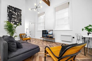 A modern living room with a gray sofa, a yellow and black chair, a TV on a stand, and a potted plant.