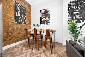 A dining area with a brick wall, wooden chairs, a wooden table, and abstract art on the walls.