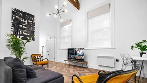 Ein modernes Wohnzimmer mit einem grauen Sofa, einem gelb-schwarzen Sessel, einem Fernseher auf einem Schrank und einem Blumentopf.