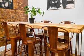 A rustic dining area with a wooden table and metal chairs, a potted plant, and a brick wall. - Luxury 2 Bedroom Apartment - Free Netflix - Wolverhampton Centre (Wolverhampton)