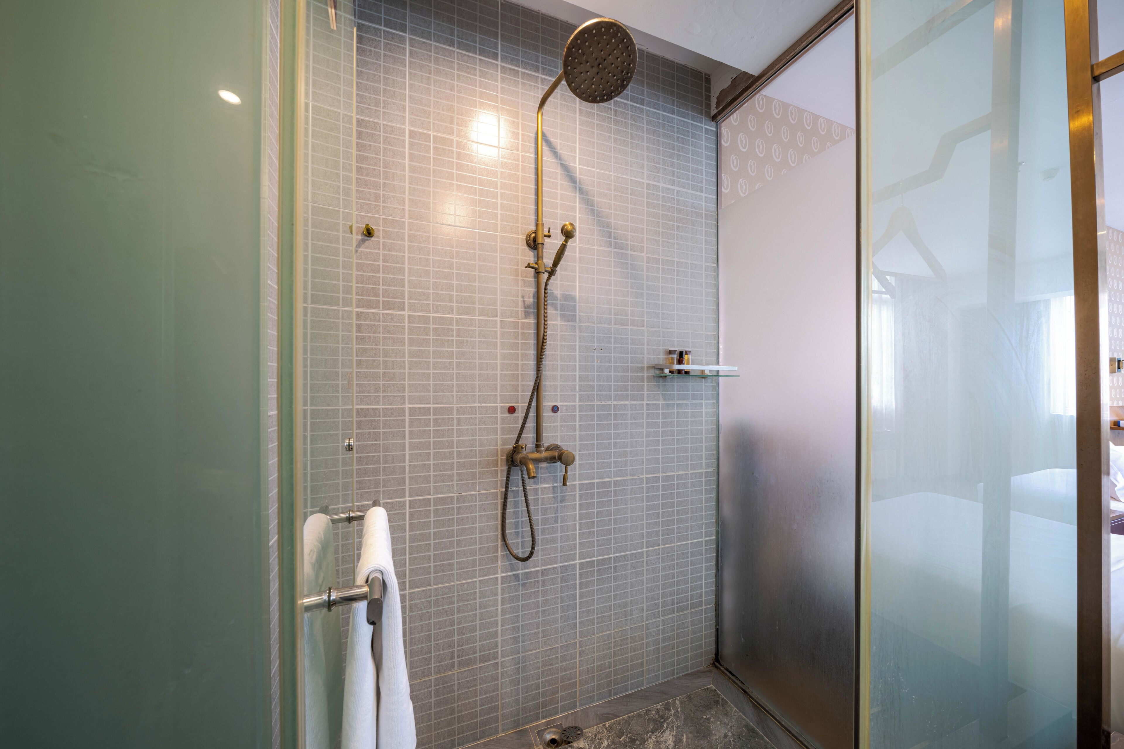 A glass-enclosed shower with a handheld showerhead and a wall-mounted faucet.