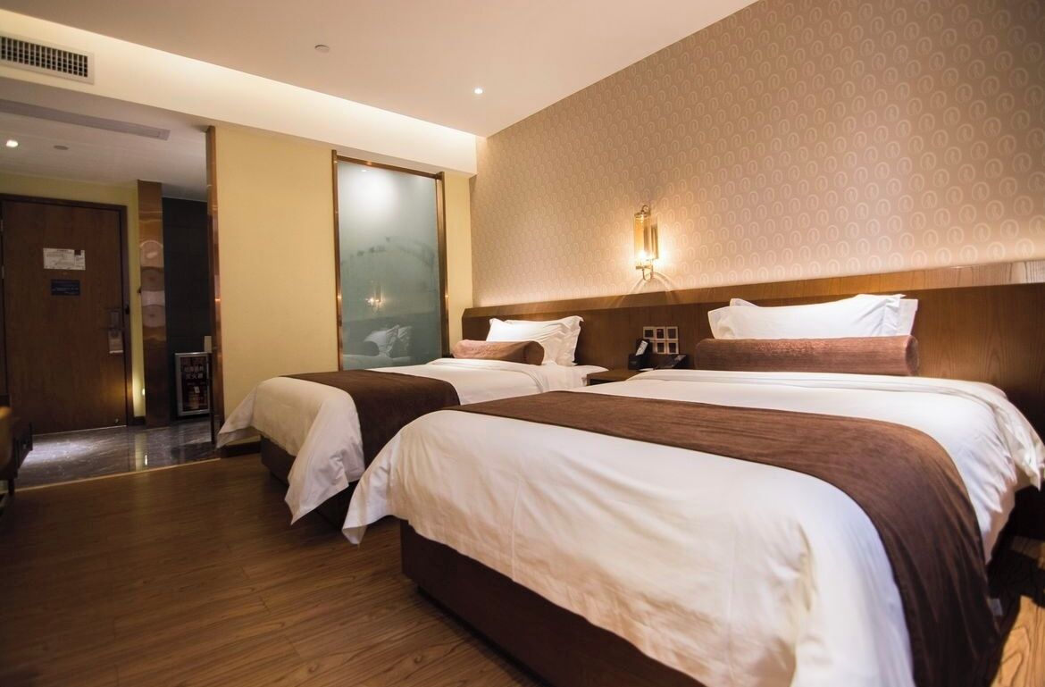 Une chambre d’hôtel avec deux lits, un plancher en bois, une grande fenêtre et un luminaire fixé au mur.
