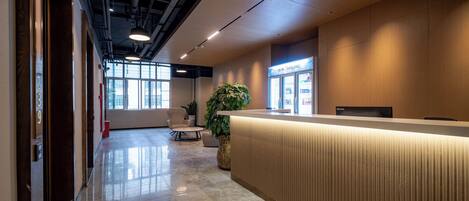 A modern reception area with a marble floor, a reception desk, a potted plant, and a seating area with chairs.