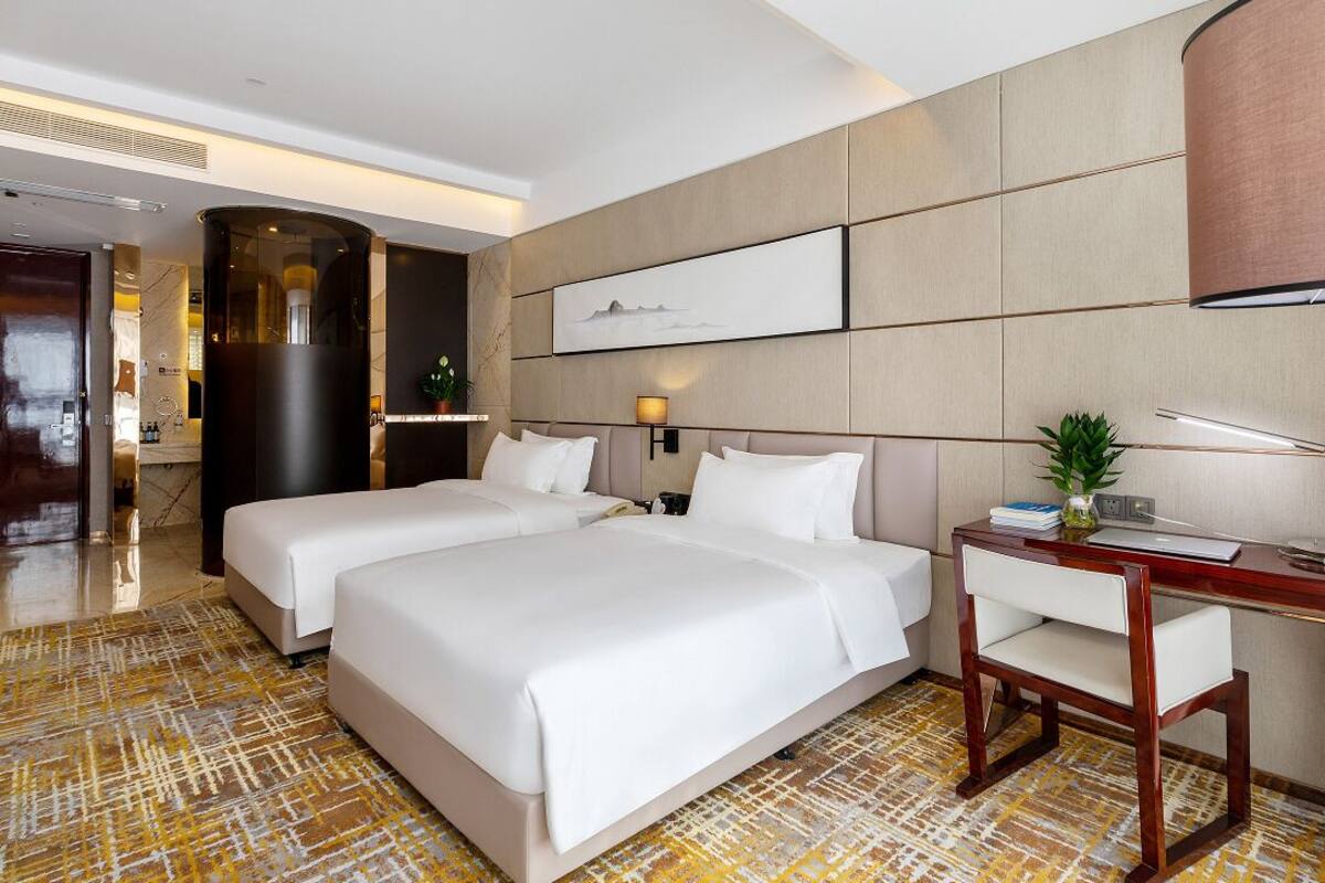 Une chambre d’hôtel avec deux lits, un bureau, une chaise, une lampe et un tableau au mur.