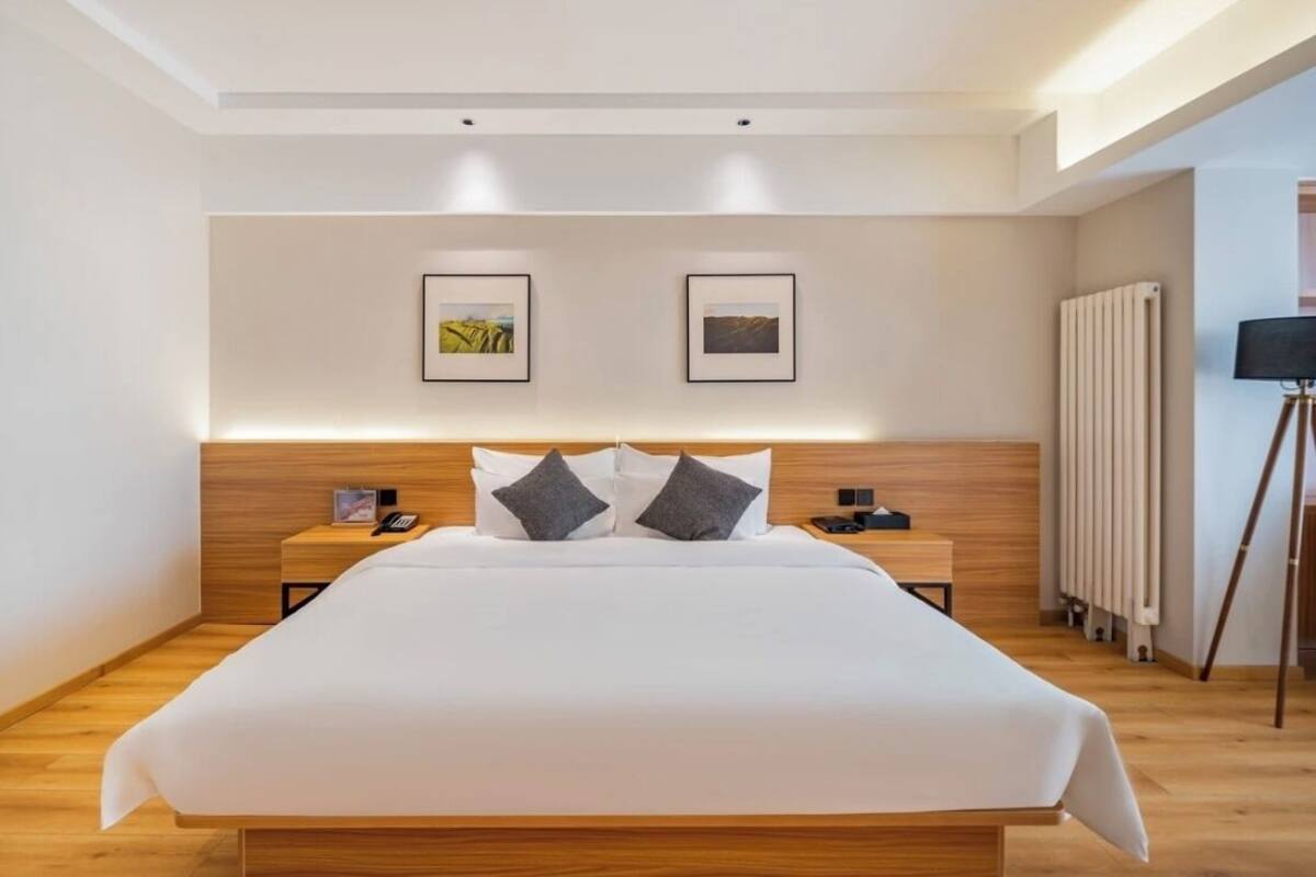 Une chambre d’hôtel moderne avec un grand lit, une tête de lit en bois, des tables de chevet et des tableaux encadrés au mur.