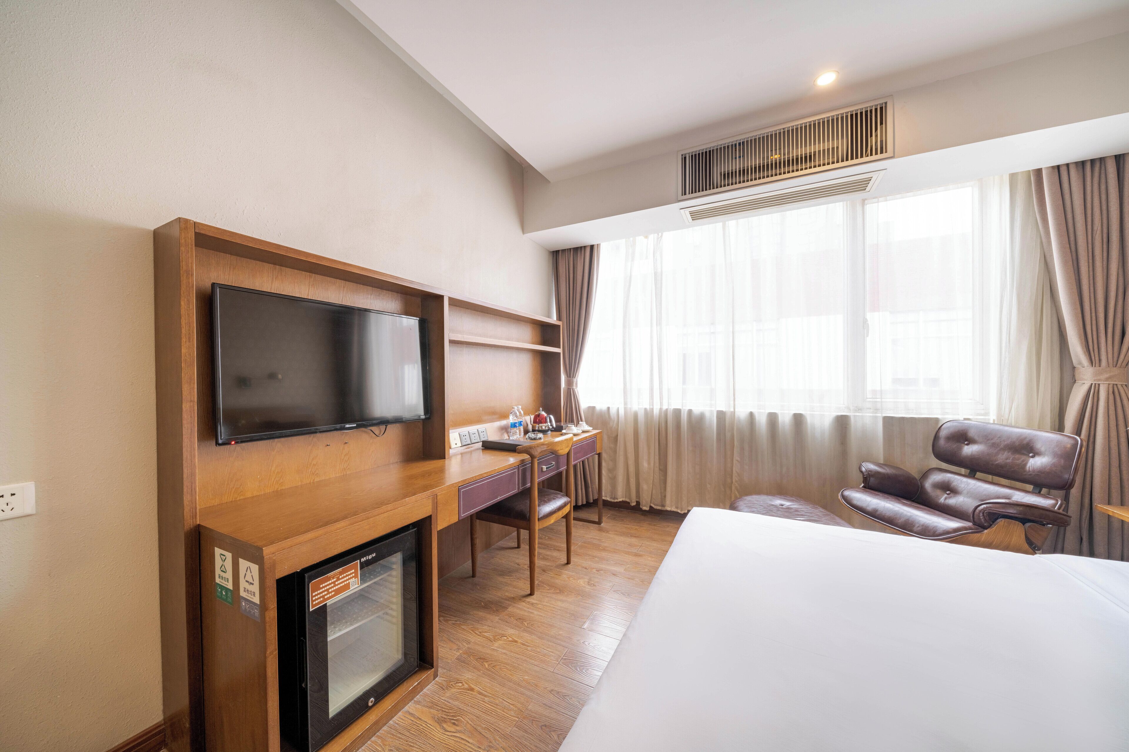 Une chambre d’hôtel avec un lit, un bureau avec une télévision, une chaise et une fenêtre avec des rideaux.