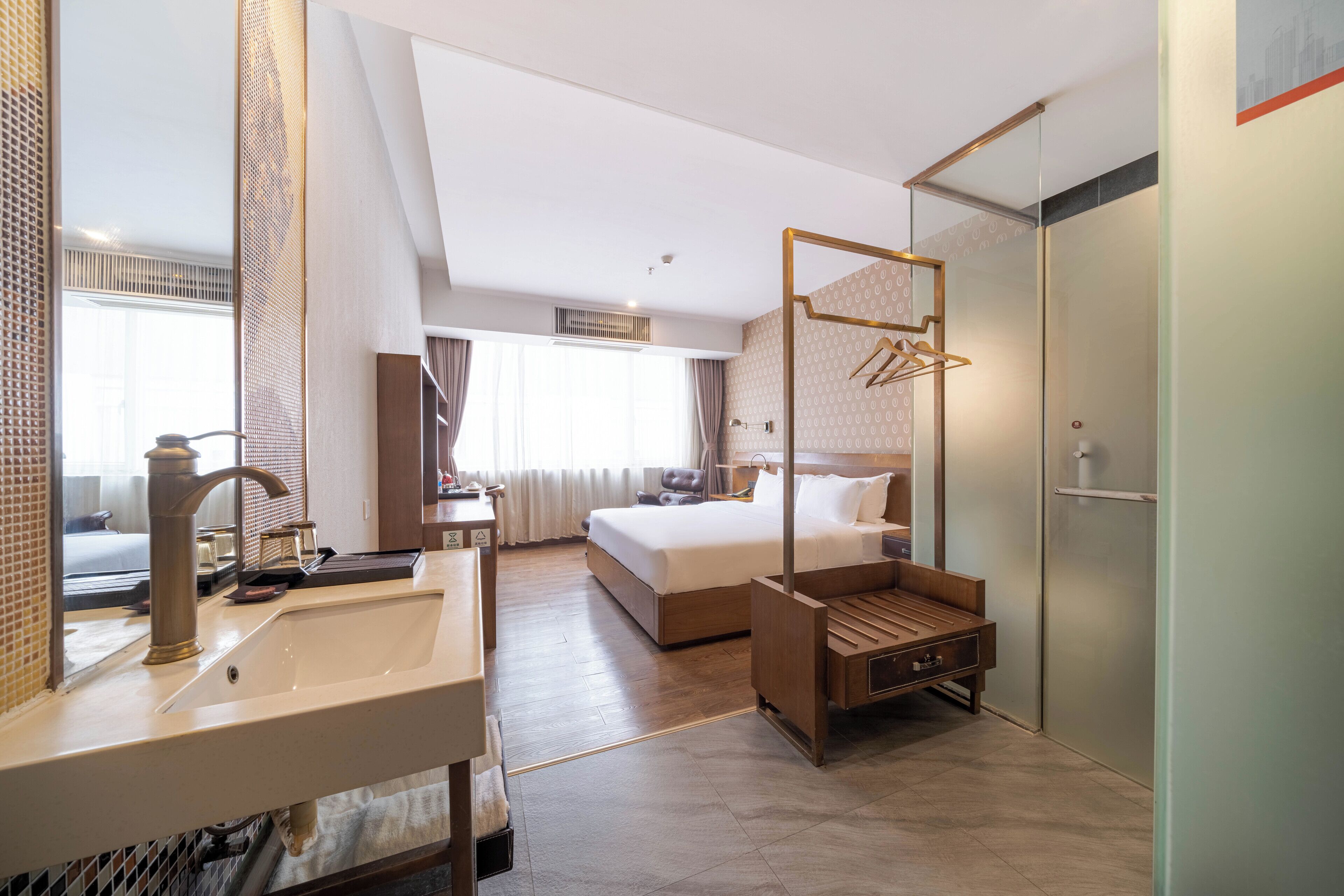 Una habitación de hotel moderna con una cama grande, una mesita de noche de madera, un lavamanos integrado y un espejo amplio.