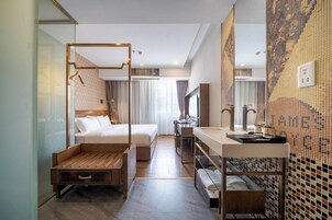 Una camera d'albergo moderna con un grande letto, una panca in legno, una scrivania e un bagno con pareti piastrellate.