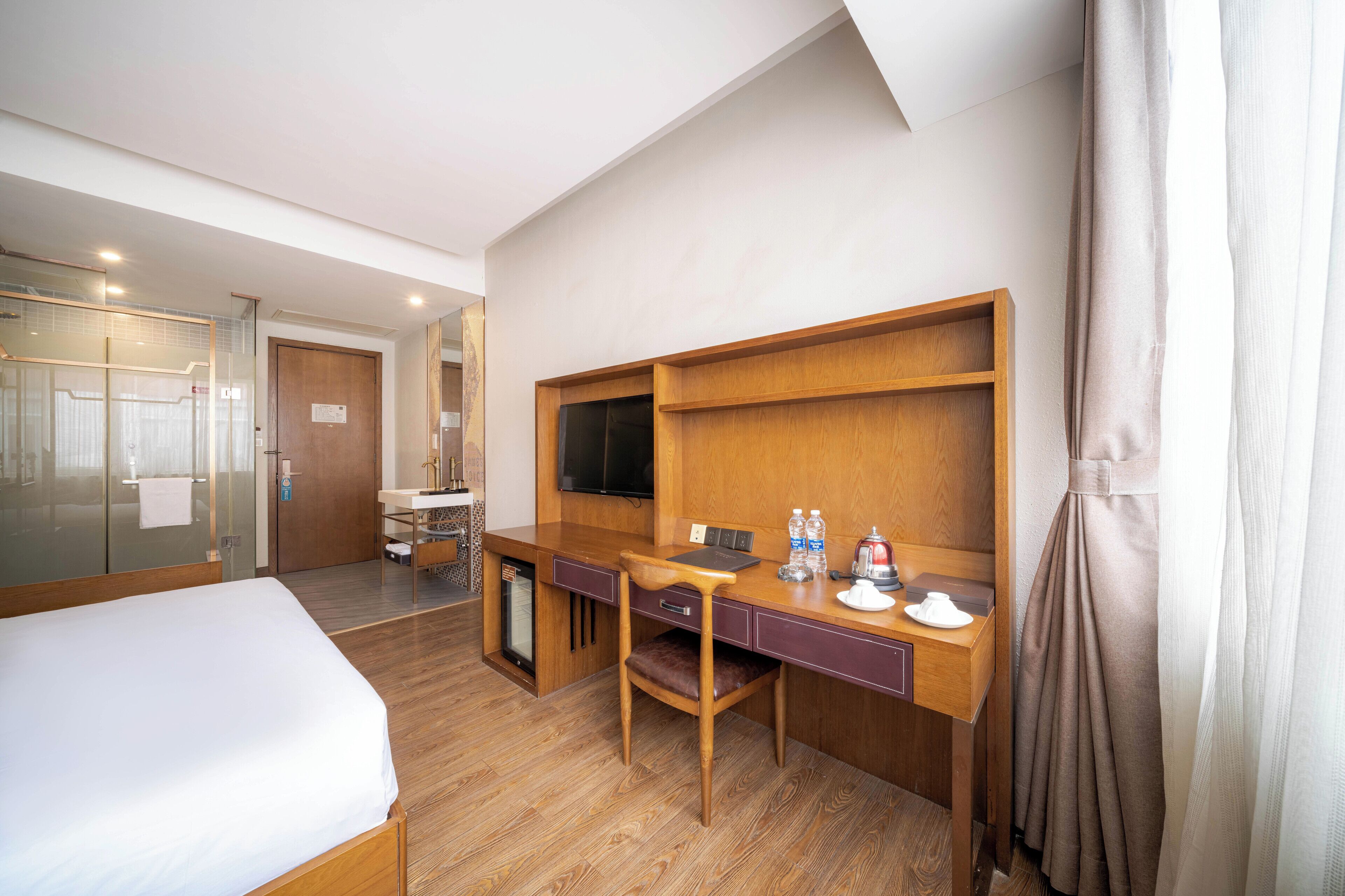 A hotel room with a bed, a desk with a chair, a television, and a minibar.