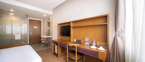 A hotel room with a bed, a desk with a chair, a television, and a minibar.