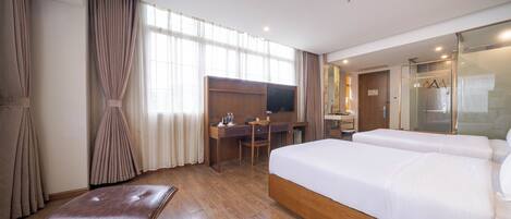 A hotel room with a large bed, a desk, a chair, a bench, and a shower area.
