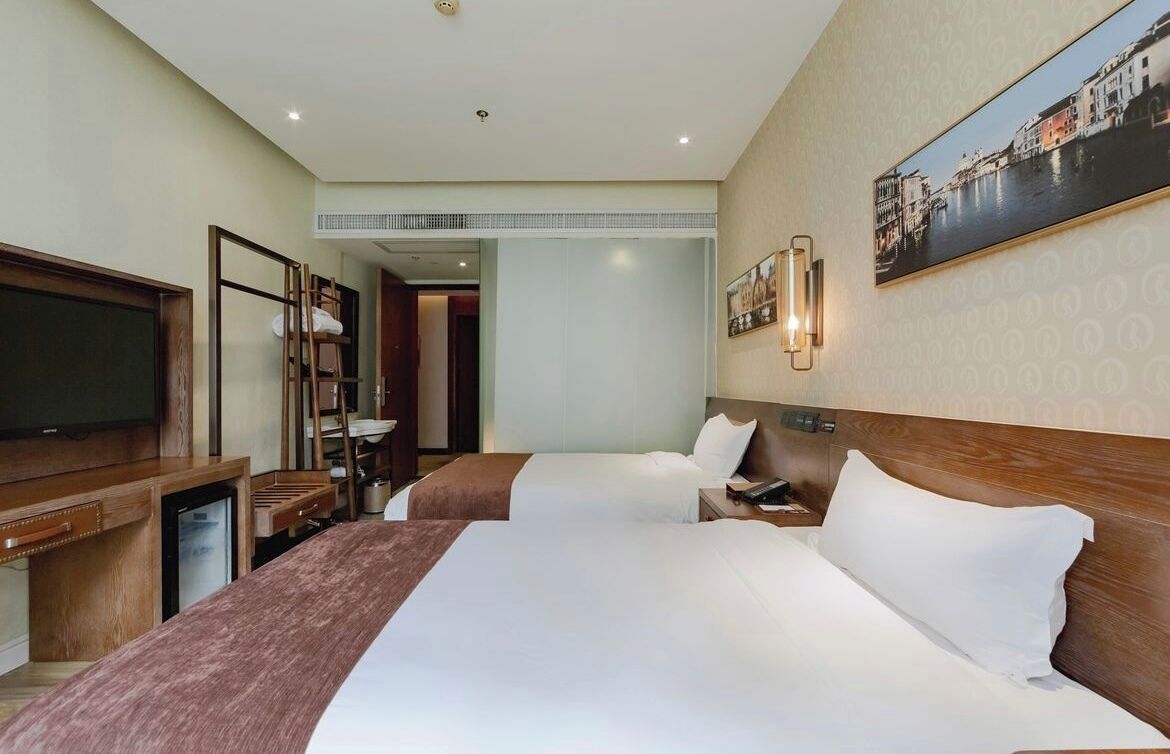 A hotel room with two beds, a TV, a desk, and a painting on the wall.