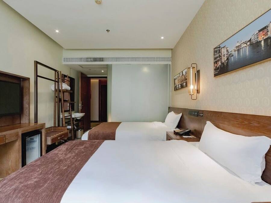 A hotel room with two beds, a TV, a desk, and a painting on the wall.