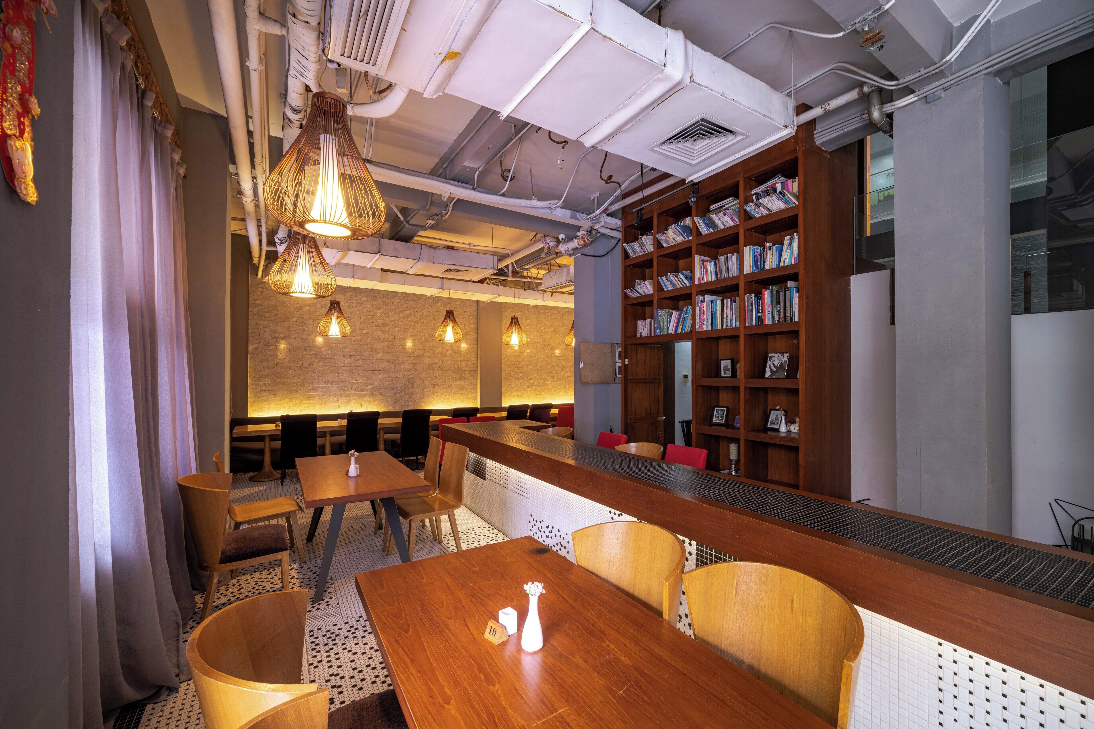 Un restaurante moderno con mesas y sillas de madera, iluminación colgante y una estantería llena de libros.
