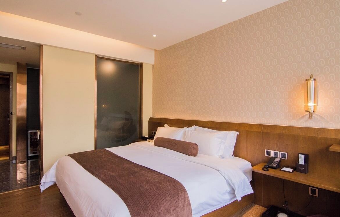 Een hotelkamer met een groot bed, een nachtkastje met een telefoon en een wandlamp.