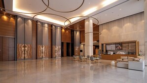 A spacious lobby with a reception desk, seating area, and a modern design with wood paneling and a marble floor. - Xingyi Chain Hotel Jiangxia Metro Station (Guangzhou)