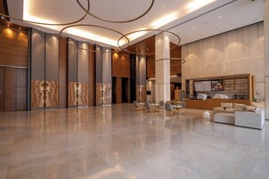 Un'ampia hall con reception, area lounge e design moderno caratterizzato da pannelli in legno e pavimento in marmo.