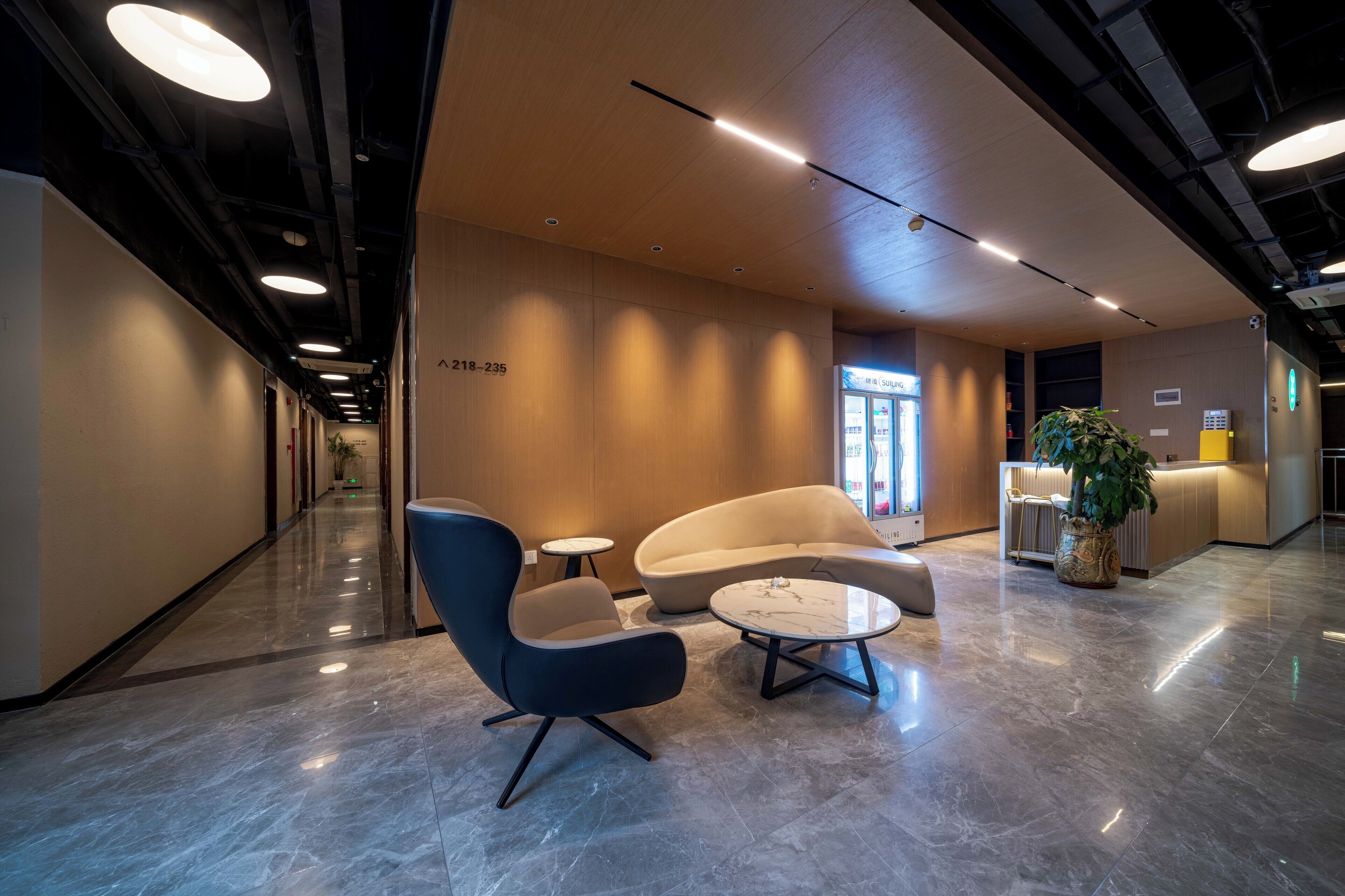 A modern lobby with a reception desk, seating area, and a plant.