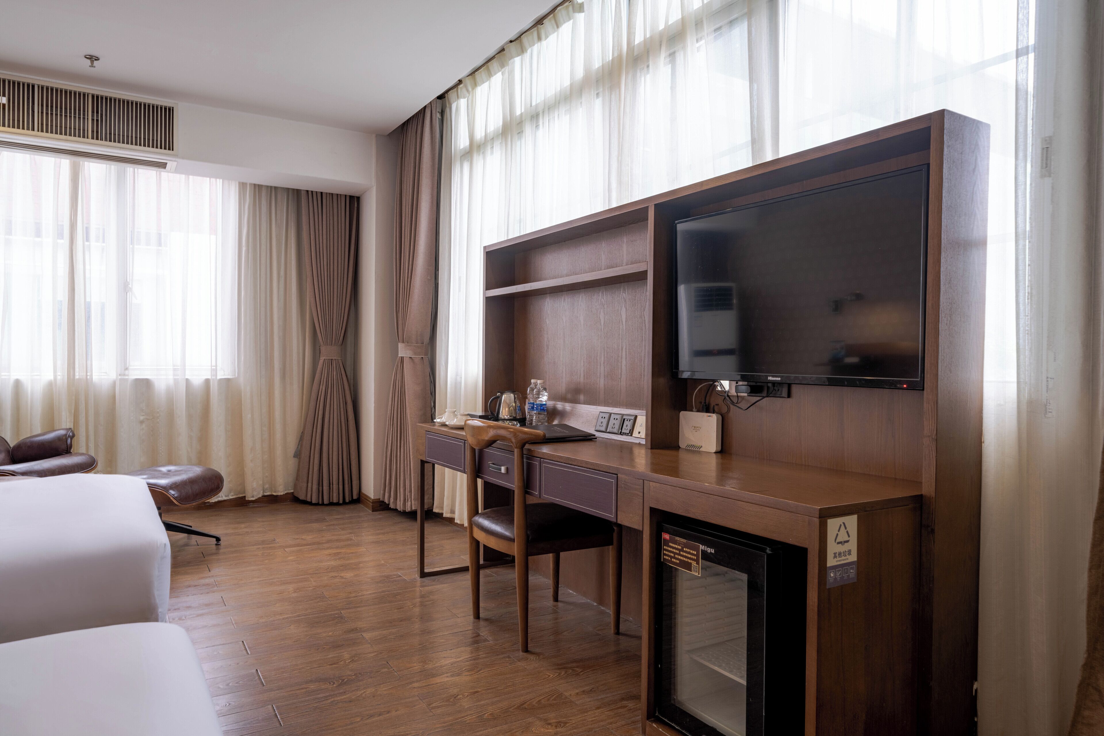 A hotel room with a wooden desk, a chair, a bed, and a television.