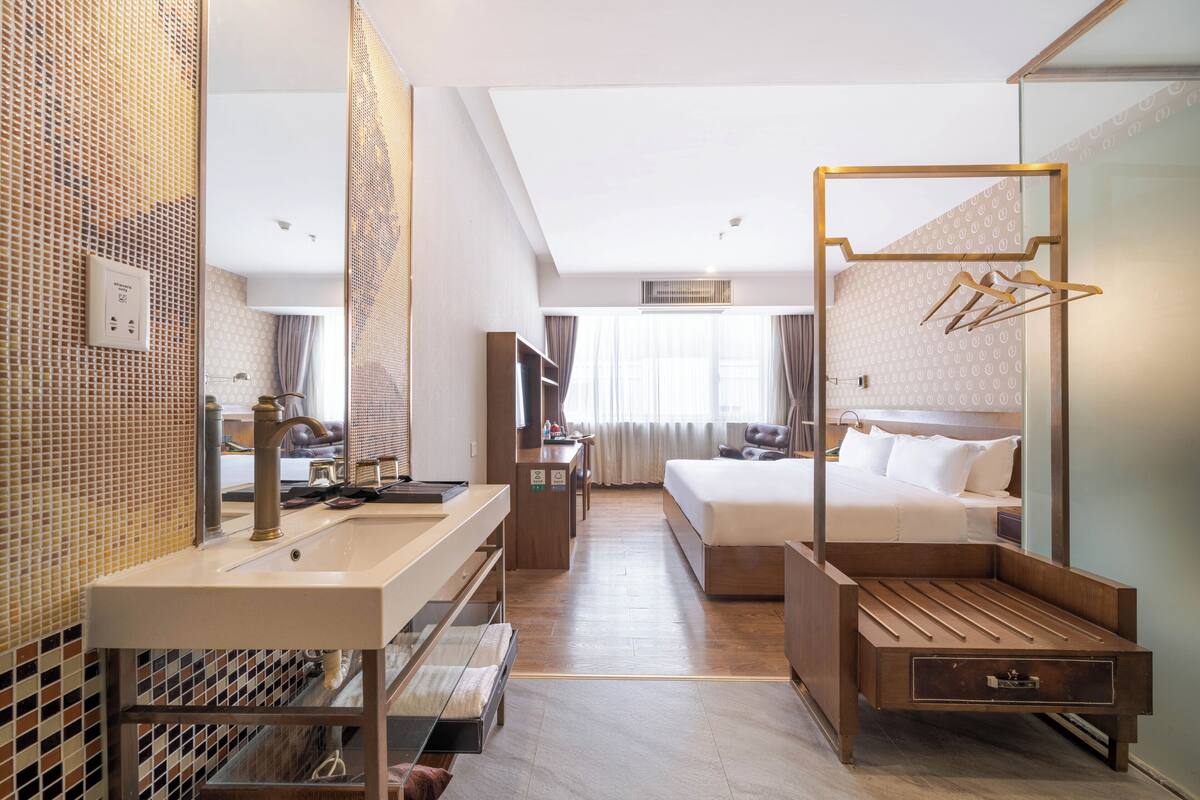 Une chambre d’hôtel avec un grand lit, une table de chevet, un miroir, un lavabo et une armoire.