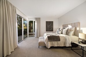 Un dormitorio moderno con una cama grande, una mesita de noche y vistas al exterior a través de un ventanal corredero.