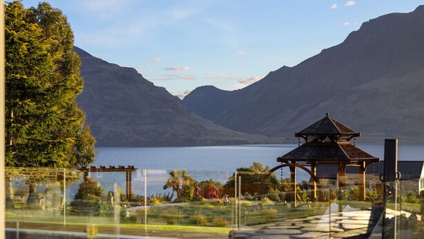 A serene lakeside view with a gazebo, a swimming pool, and mountainous terrain in the background.