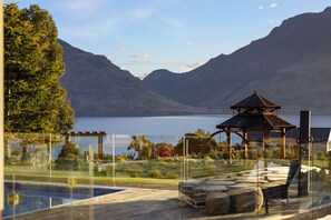 Una vista serena de un lago con un pabellón, piscina y terreno montañoso al fondo.
