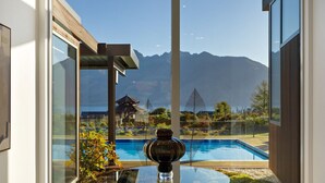 A modern outdoor area with a glass table, a decorative vase, and a view of a swimming pool and mountains.