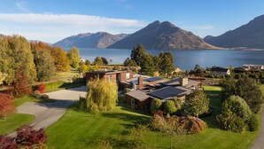 A modern house with solar panels, surrounded by a well-maintained garden and a view of mountains and a lake.