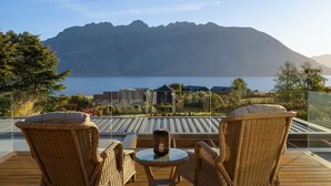 A terrace with wicker chairs and a table overlooking a lake with mountains in the background.