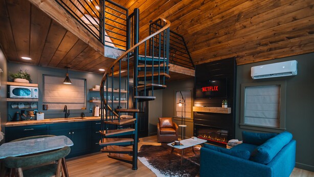 A modern kitchen with a built-in microwave, a dining table with chairs, and a spiral staircase leading to an upper level. - Edinburgh Escape | Hot Tub, Sauana + Fire Pit + Grill (Apple Creek)