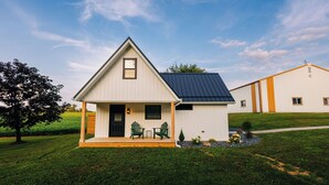 A small, single-story house with a gabled roof, a front porch with two chairs, and a small garden area. - Edinburgh Escape | Hot Tub, Sauana + Fire Pit + Grill (Apple Creek)