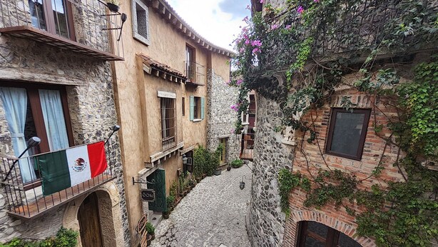A narrow cobblestone street flanked by stone buildings with balconies, a flag, and potted plants. - Castello di Carlo - Suite Carlo VII (Val'Quirico)