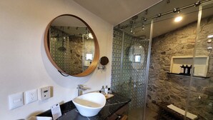 Een badkamer met een witte wastafel, een ronde spiegel en een douchecabine van glas.