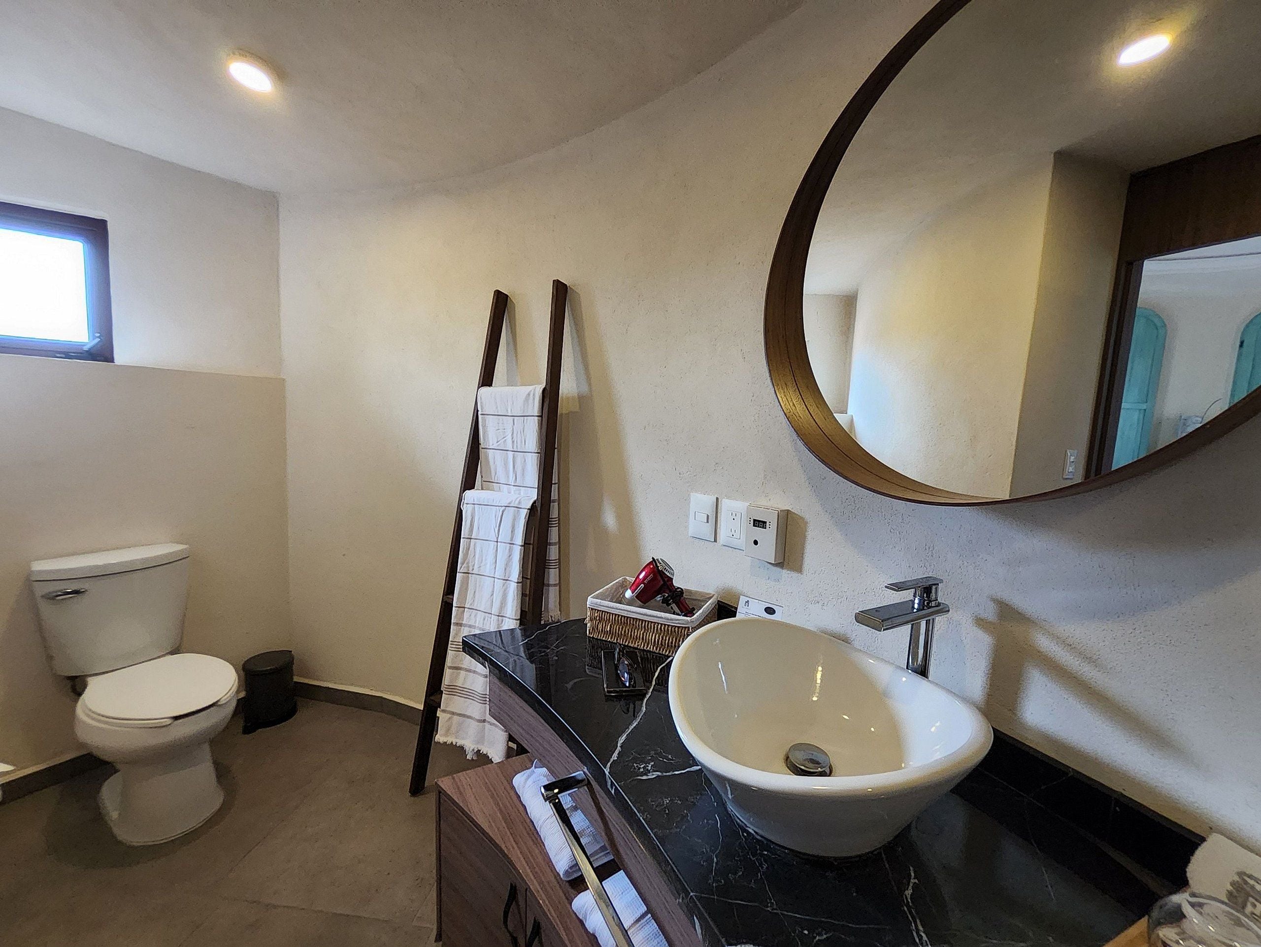 Un baño con inodoro, lavamanos, espejo y toallero.