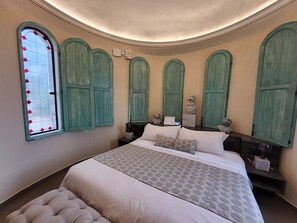 A bedroom with a large bed, green shutters, a decorative window, and a small table with a lamp. - Castello di Carlo - Suite Carlo VII (Val'Quirico)
