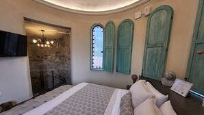 Een slaapkamer met een bed, een stenen muur, een raam met luiken en een aan de muur bevestigde televisie.