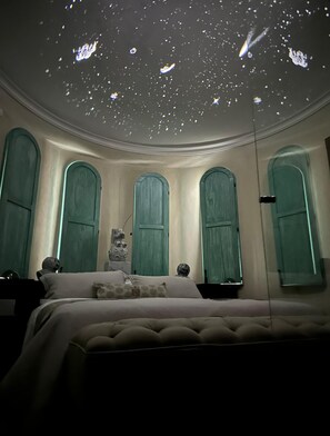 A bedroom with a curved ceiling, three arched windows, and a bed with a tufted headboard.