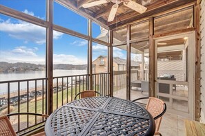 Ein überdachter Balkon mit Tisch und Stühlen, mit Blick auf einen See und Gebäude.