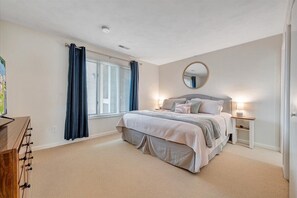 Ein Schlafzimmer mit einem Bett, einem Nachttisch, einem Spiegel und einem Fenster mit Vorhängen.