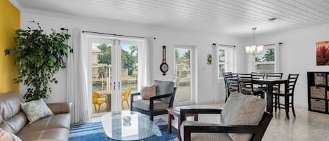 A spacious living room with a glass coffee table, leather sofa, and a dining area with a wooden table and chairs.