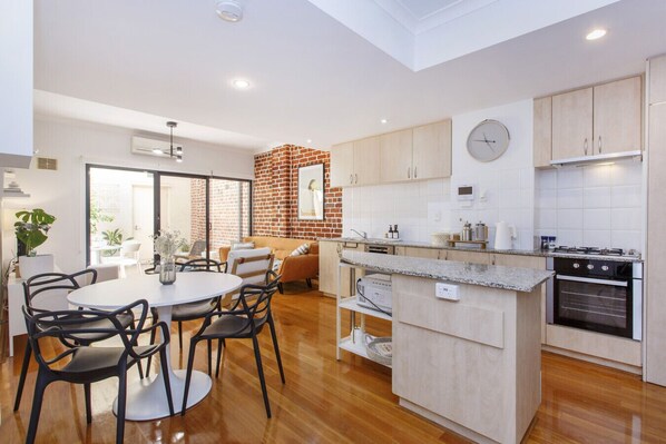 A modern kitchen with a central island, wooden cabinets, and a built-in oven. - West End Courtyard Retreat (Fremantle)
