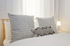A bed with white bedding and two pillows, one striped and one with a black and white pattern. - West End Courtyard Retreat (Fremantle)